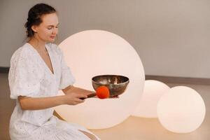 Portrait of a female yoga teacher playing a Tibetan bowl or singing a bell in the gym during a yoga retreat photo