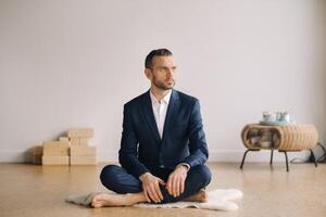 A man in a strict suit does Yoga while sitting in a fitness room photo