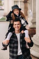 A cheerful Daughter is sitting on dad's shoulders and walking around the autumn city photo