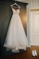 White wedding dress hanging on a hanger in a hotel room photo