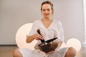 Portrait of a female yoga teacher playing a Tibetan bowl or singing a bell in the gym during a yoga retreat photo