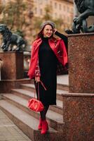 A beautiful stylish woman dressed in an elegant red coat with a stylish red handbag in the autumn city photo