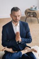 A man in a strict suit does Yoga while sitting in a fitness room photo