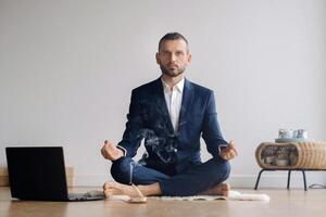 A man in a formal suit meditates while sitting in a fitness room with a laptop photo