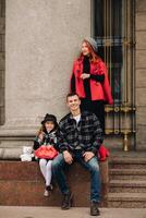 un elegante familia de Tres paseos mediante el otoño ciudad posando para un fotógrafo . papá, mamá y hija en el otoño ciudad foto