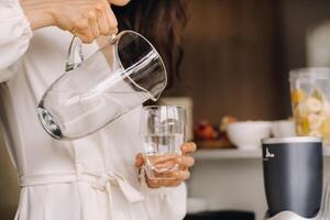 Close-up of the hands of a girl in the kitchen who pours clean water into a glass. Healthy eating photo