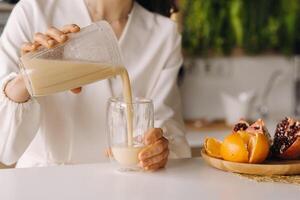 de cerca de un muchachas manos torrencial un Fresco Fruta cóctel de bananas y un naranja en el cocina. dieta para peso pérdida foto