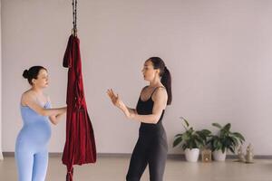 Pregnant girl. A woman with a trainer does yoga in a hammock in the gym. The concept of a healthy lifestyle, motherhood photo