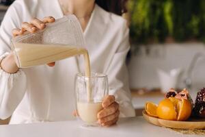 de cerca de un muchachas manos torrencial un Fresco Fruta cóctel de bananas y un naranja en el cocina. dieta para peso pérdida foto