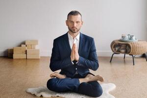 A man in a strict suit does Yoga while sitting in a fitness room photo