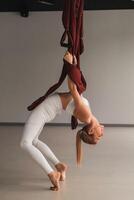 A girl in white sportswear does yoga on a hanging hammock in the fitness room photo