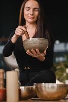 A woman in the lotus position using a singing bowl indoors . Relaxation and meditation. Sound therapy, alternative medicine. Buddhist healing practices photo