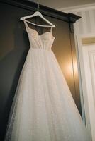 White wedding dress hanging on a hanger in a hotel room photo