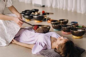 The copper singing bowl of the Nepalese Buddha in the spa. A young beautiful woman is doing a massage with singing bowls in a spa salon against the backdrop of a waterfall photo