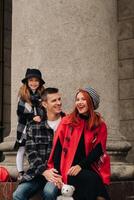 un elegante familia de Tres paseos mediante el otoño ciudad posando para un fotógrafo . papá, mamá y hija en el otoño ciudad foto