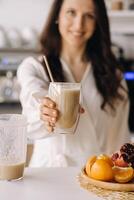 un contento sonriente sano mujer tiene preparado un Fruta cóctel y da eso a usted mientras en pie a hogar en el cocina.saludable comiendo foto