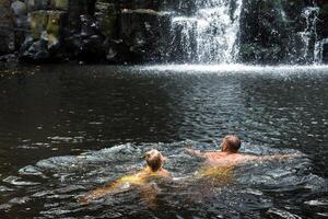 A man and a girl are swimming in a waterfall. People at the cave waterfall. Bathing photo