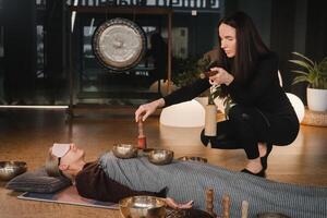 A young beautiful woman is doing a massage with singing bowls and a koshi bell to another girl. Sound therapy photo