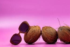 three whole coconuts and wooden glasses on a pink background photo