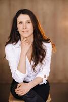 Portrait of a happy young brunette woman in a white shirt sitting on a chair photo