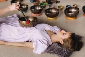 The copper singing bowl of the Nepalese Buddha in the spa. A young beautiful woman is doing a massage with singing bowls in a spa salon against the backdrop of a waterfall photo