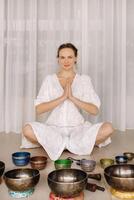 A woman sits with Tibetan bowls in the lotus position before doing yoga in the gym photo