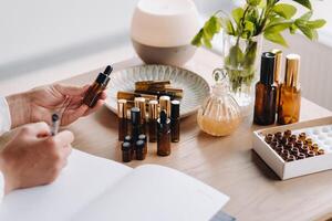 Close-up of female hands holding a bottle of essential oil and writing an entry in a notebook, aromatherapy photo