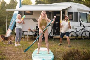 the family is resting next to their mobile home. My daughter is standing with a paddle on a sup board, and her parents pour water on her photo