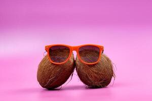 Two whole coconuts and orange glasses on a pink background. photo