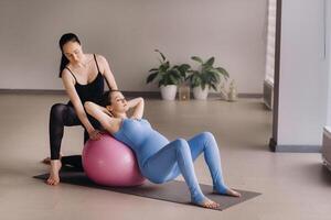 Pregnant woman with a trainer during fitness classes with a ball photo