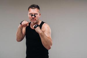 on a gray background stands a battered man in a black T shirt looking like a fighter and preparing for a fight photo