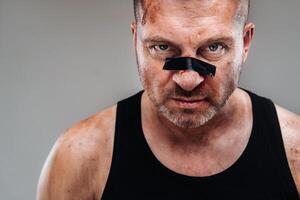 on a gray background stands a battered man in a black T shirt looking like a fighter and preparing for a fight photo