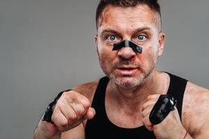 on a gray background stands a battered man in a black T shirt looking like a fighter and preparing for a fight photo