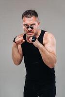 on a gray background stands a battered man in a black T shirt looking like a fighter and preparing for a fight photo