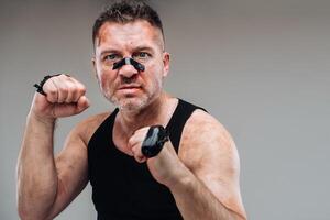 on a gray background stands a battered man in a black T shirt looking like a fighter and preparing for a fight photo