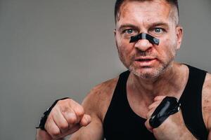 on a gray background stands a battered man in a black T shirt looking like a fighter and preparing for a fight photo