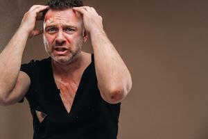 Against a gray background stands a battered angry man in a black T-shirt with wounds photo