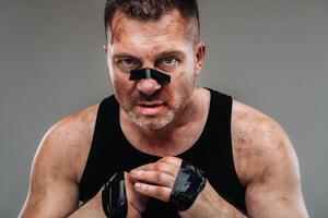 on a gray background stands a battered man in a black T shirt looking like a fighter and preparing for a fight photo