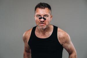 on a gray background stands a battered man in a black T shirt looking like a fighter and preparing for a fight photo