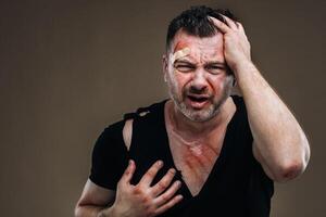 Against a gray background stands a battered angry man in a black T-shirt with wounds photo