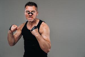 on a gray background stands a battered man in a black T shirt looking like a fighter and preparing for a fight photo