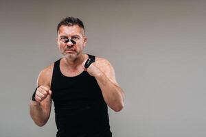 on a gray background stands a battered man in a black T shirt looking like a fighter and preparing for a fight photo