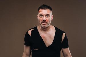 Against a gray background stands a battered angry man in a black T-shirt with wounds photo