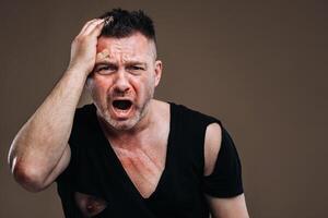 Against a gray background stands a battered angry man in a black T-shirt with wounds photo