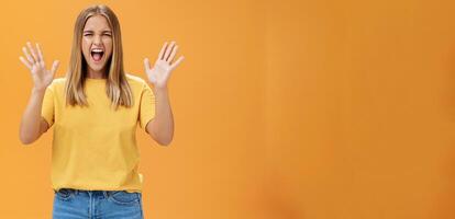 mujer liberando estrés Gritando con alegría y Placer gesticulando con elevado brazos siendo atrevido y rebelde no temeroso a espectáculo emociones en pie apasionado y expresivo en contra naranja antecedentes foto