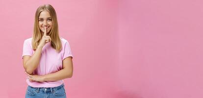 shh mantener eso secreto. retrato de carismático alegre gordito niña con bronceado piel y justa pelo demostración silenciar gesto con índice dedo terminado boca sonriente ocultación sorpresa posando terminado rosado antecedentes foto