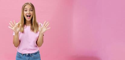 Amused and surprised excited attractive young caucasian female in casual t-shirt gesturing with spread fingers over chest smiling broadly with amazement looking at camera telling awesome news photo