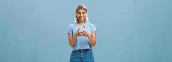 niña teniendo gracioso conversación, Hablando con amigo vía vídeo mensajes en inalámbrico auriculares participación teléfono inteligente en ambos manos sonriente felizmente a dispositivo pantalla siendo entretenido y divertido foto