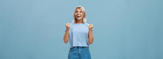 suerte contento niña triunfando y riendo desde felicidad victorioso primero sitio apretando puños en éxito gesto sonriente en general celebrando victoria con entusiasmo y emoción terminado azul antecedentes foto