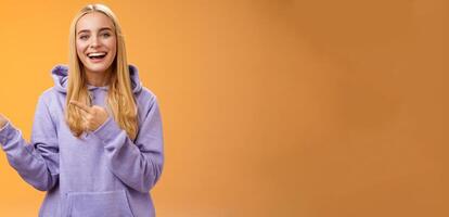 Charismatic firendly good-looking blond young female student pointing left discussing awesome new restaurant suggesting friend go check out laughing smiling happily, orange background photo